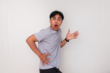 Funny young Asian man standing and showing a surprised face with a shocked gesture, isolated on...