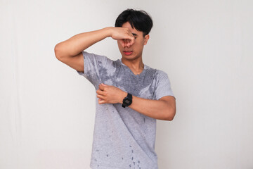 Young Asian man sweating and closing his nose with a disgusted face due to body odor, isolated on...