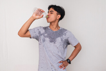 oung Asian man sweating while drinking a bottle of mineral water, isolated on white background....