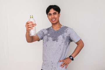 Confident young Asian man sweating and smiling while showing a bottle of water to the camera,...
