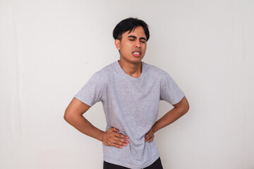 Unhealthy young Asian man holding his stomach with a painful expression, suffering from abdominal...