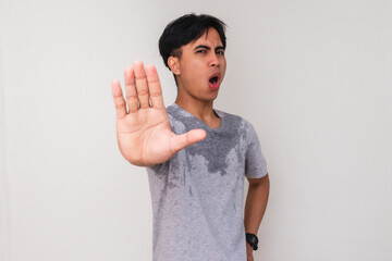 Portrait of a young Asian man sweating heavily with a serious face, making a stop hand gesture due...