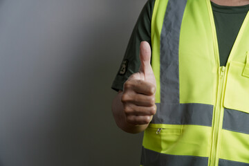 A person wearing a safety vest gives a clear thumbs up gesture