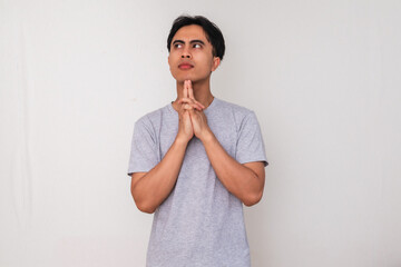 Portrait of a young Asian man thinking seriously with hand on chin and eyes looking up, isolated on...