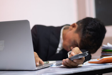 Asian businessman sitting at desk, looking thoughtful and stressed. There are many financial...