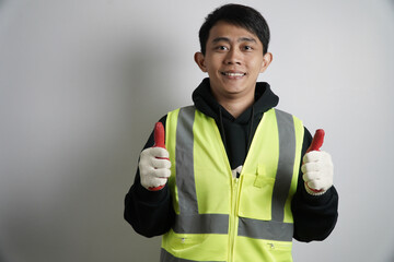Young Asian Man in Safety Vest Giving Thumbs Up, Asian male worker in a reflective safety vest...