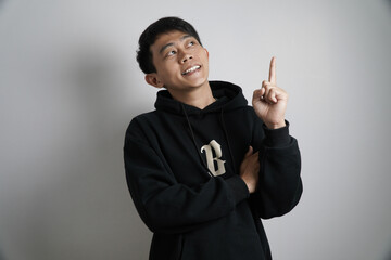 A contemplative young Asian man in a black hoodie looks up and points his index finger, suggesting...