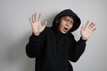 Scared Young Asian Man in Hoodie with Defensive Stop Gesture