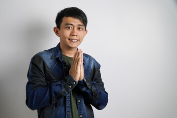 Smiling young Asian man gesturing traditional greeting isolated over gray background