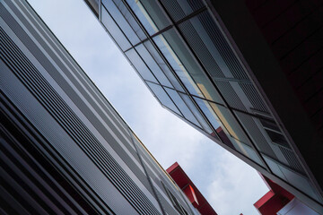 Low-angle view capturing the striking geometric interplay of modern building facades with reflective glass and contrasting red elements against the sky.