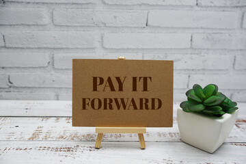 Pay It Forward text message with easel stand on wooden background