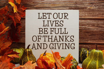 Let Our Lives Be Full Of Thanks And Giving text with maple leaf decoration on wooden background