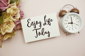 Enjoy Life Today text on paper card with alarm clock on pink background