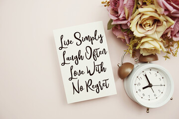 Live Simply Laugh Often Love With No Regret text on paper card with alarm clock on pink background