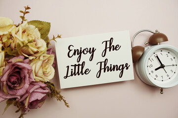 Enjoy The Little Things text on paper card with alarm clock on pink background