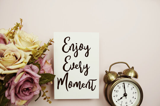 Naklejki Enjoy Every Moment text on paper card with alarm clock on pink background