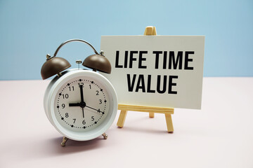 Life Time Value text on paper card with alarm clock on pink background