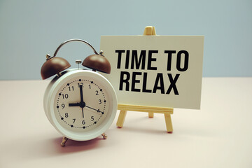 Time To Relax text on paper card with alarm clock on pink background