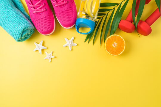 Summer fitness background with dumbbells, bottle of water, sport shoes and palm leaf. Top view with copy space