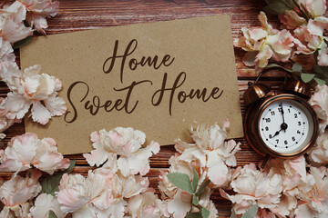 Home Sweet Home text with alarm clock and flowers decoration on wooden background