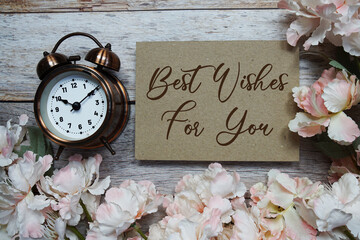 Best Wishes For You text with alarm clock and flowers decoration on wooden background