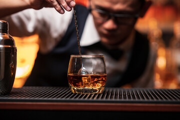 Bartender is pouring whiskey into a glass a customer's glass.