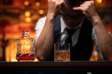 Handsome businessman or young man sits, drinks whiskey, looks stressed and sad.