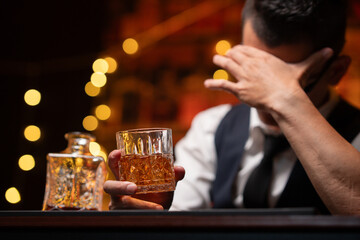 Handsome businessman or young man sits, drinks whiskey, looks stressed and sad.