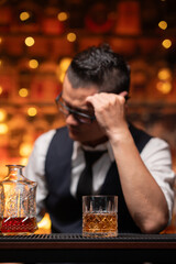 Handsome businessman or young man sits, drinks whiskey, looks stressed and sad.