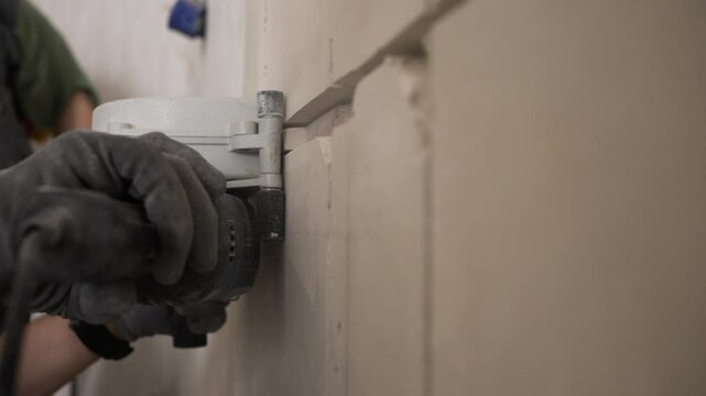 Professional construction worker wearing protective gloves uses a wall chaser to carefully cut a precise groove into a plastered wall. Preparing the space for electrical wiring or cable installation
