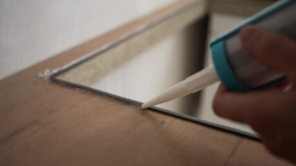 Skilled construction worker applying silicone sealant around electric stove's perimeter, creating precision airtight seal during kitchen renovation project - Powered by Adobe
