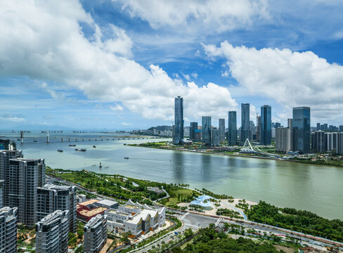Beautiful panoramic landscape of a coastal city with modern high-rise buildings lining the riverfront under a bright sky with white clouds in Zhuhai. - Powered by Adobe