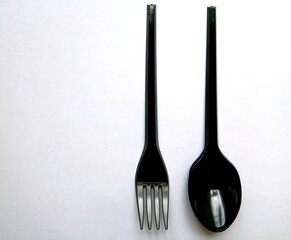 Black plastic spoons and forks arranged on a white background.