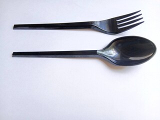 Black plastic spoons and forks arranged on a white background.