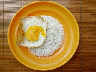 Fried eggs and white rice are served on plastic plates on a wooden table. A simple and cheap menu.