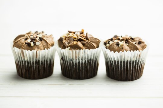 Naklejki Chocolate cupcakes are showing in flat design on white table with liners, frosting and toppings