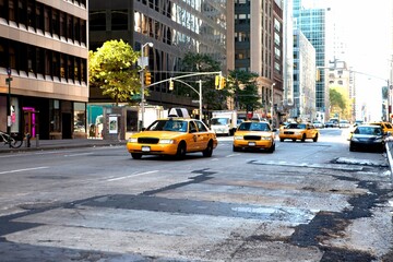 Yellow taxi cabs are cruising along worn downtown avenue under signals, signs by office towers
