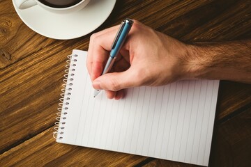 Man writing in book by coffee cup on table