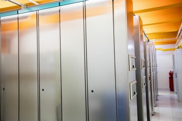 Row of tall grey cabinets is lining narrow corridor flat, with yellow ducts and red extinguisher
