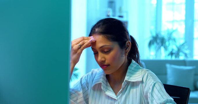 Indian businesswoman having headache while working on laptop at desk in modern cozy office, Asian young female showing stress and stiff neck symptoms while dealing with workload and physical pressure