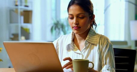 Businesswoman using phone while having coffee mug during office break, Indian Asian female professional standing at desk in cozy workspace, smiling and engaged with smartphone while holding beverage - Powered by Adobe