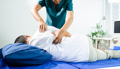 Male physiotherapist applies manual therapy on patient's back during rehab session. Spine care,...