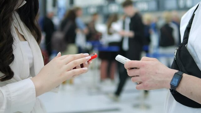 Two people are talking on their cell phones in a crowded airport. One of them is holding a red lipstick
