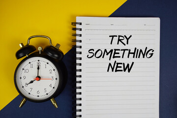 Try Something New text written on notepad with alarm clock on yellow background