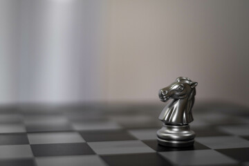 A close-up of a metallic chess knight on a black and white chessboard, emphasizing strategy and...
