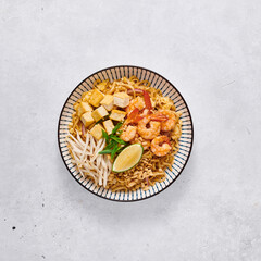 Pad Thai with shrimp, sprouts and green onions on a concrete background, top view
