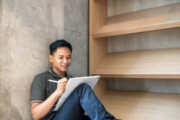 Man smiling while using a stylus and tablet, surrounded by books, portraying productivity and focus.