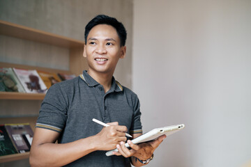 Man smiling while using a stylus and tablet, surrounded by books, portraying productivity and focus.