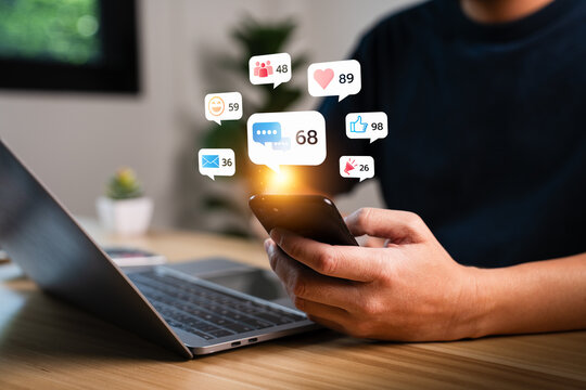 Close up of man using smartphone with social media notification icons such as like, heart, message, group, and email floating above screen, concept of digital communication and online engagement