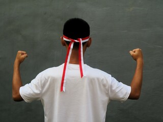 Indonesia teens in white t-shirt with red and white headband and clenched fist against grey...